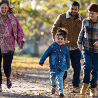 photo of hispanic dad and white mom walking outside through a park in the fall season with their daughter and son